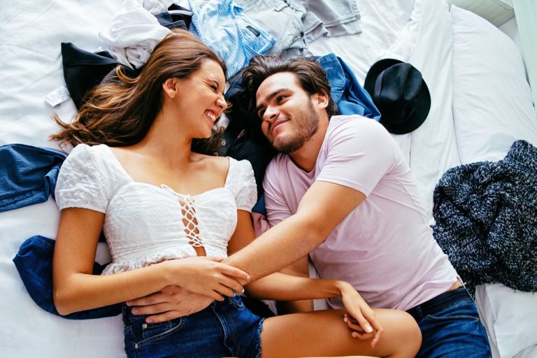 portrait of a happy young couple lying on a bed with clothes, smiling while holding each other