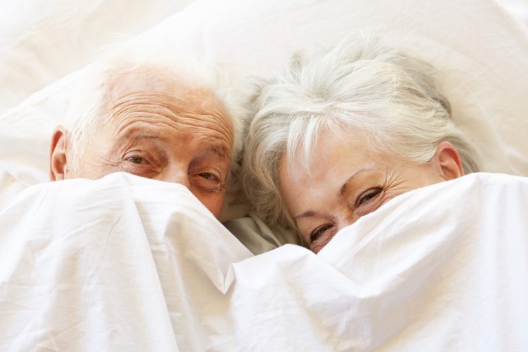 senior couple relaxing in bed hiding under sheets